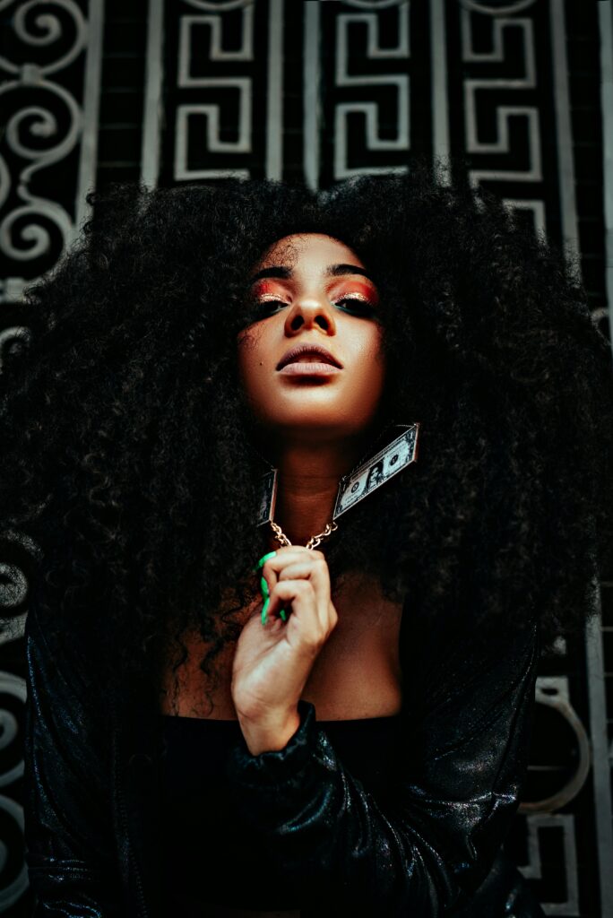 Dynamic editorial photo of a model with afro hair and bold makeup in an urban setting, exuding glamour and edge.